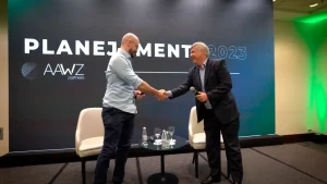 Dois executivos apertando as mãos no palco de evento corporativo.