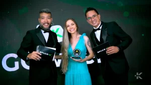 Três pessoas posando para foto em uma festa de premiação corporativa.