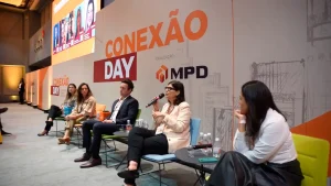 Pessoas sentadas em um palco debatendo para o público durante evento corporativo